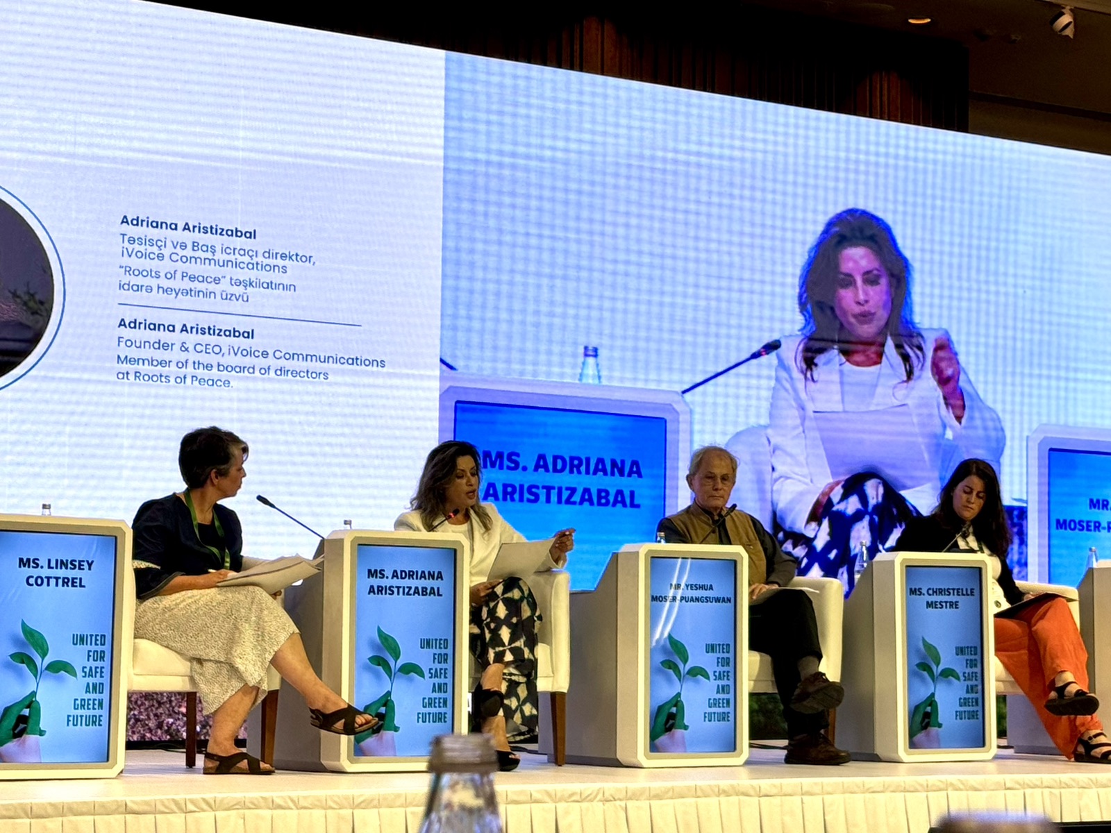 Adriana Aristizábal speaking on a panel at the International Conference on Mine Action in Baku, shown on the screen behind the stage